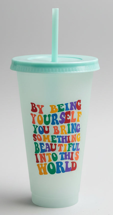 A translucent mint green plastic travel tumbler with a matching lid and straw, featuring a colorful text graphic that reads 'BY BEING YOURSELF YOU BRING SOMETHING BEAUTIFUL INTO THE WORLD'. 