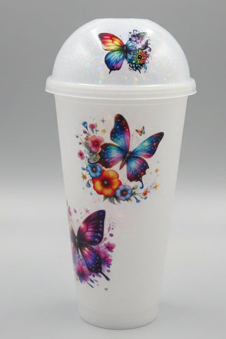 A clear plastic takeaway cup with a matching dome lid, decorated with colorful butterfly and floral designs.